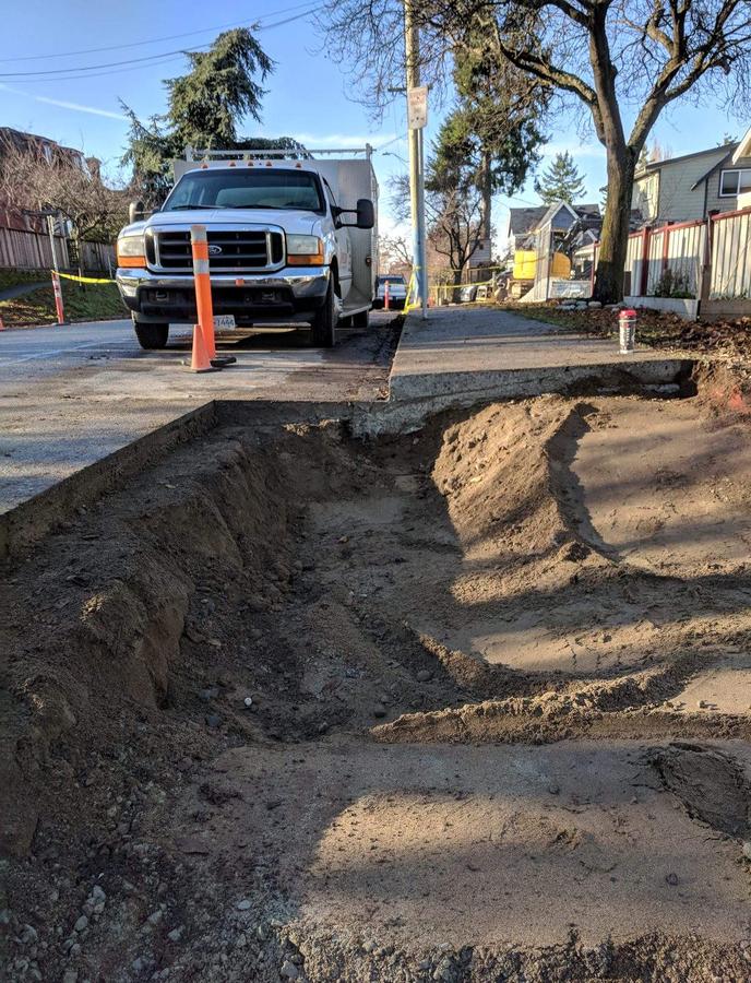 Deep service trench excavation beside a finished concrete sidewalk in Greater Victoria